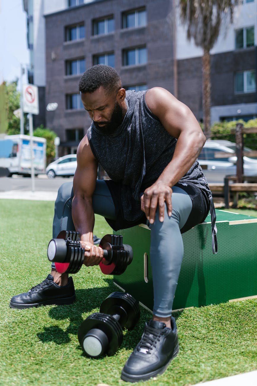 bearded man sitting on a box while lifting dumbbell